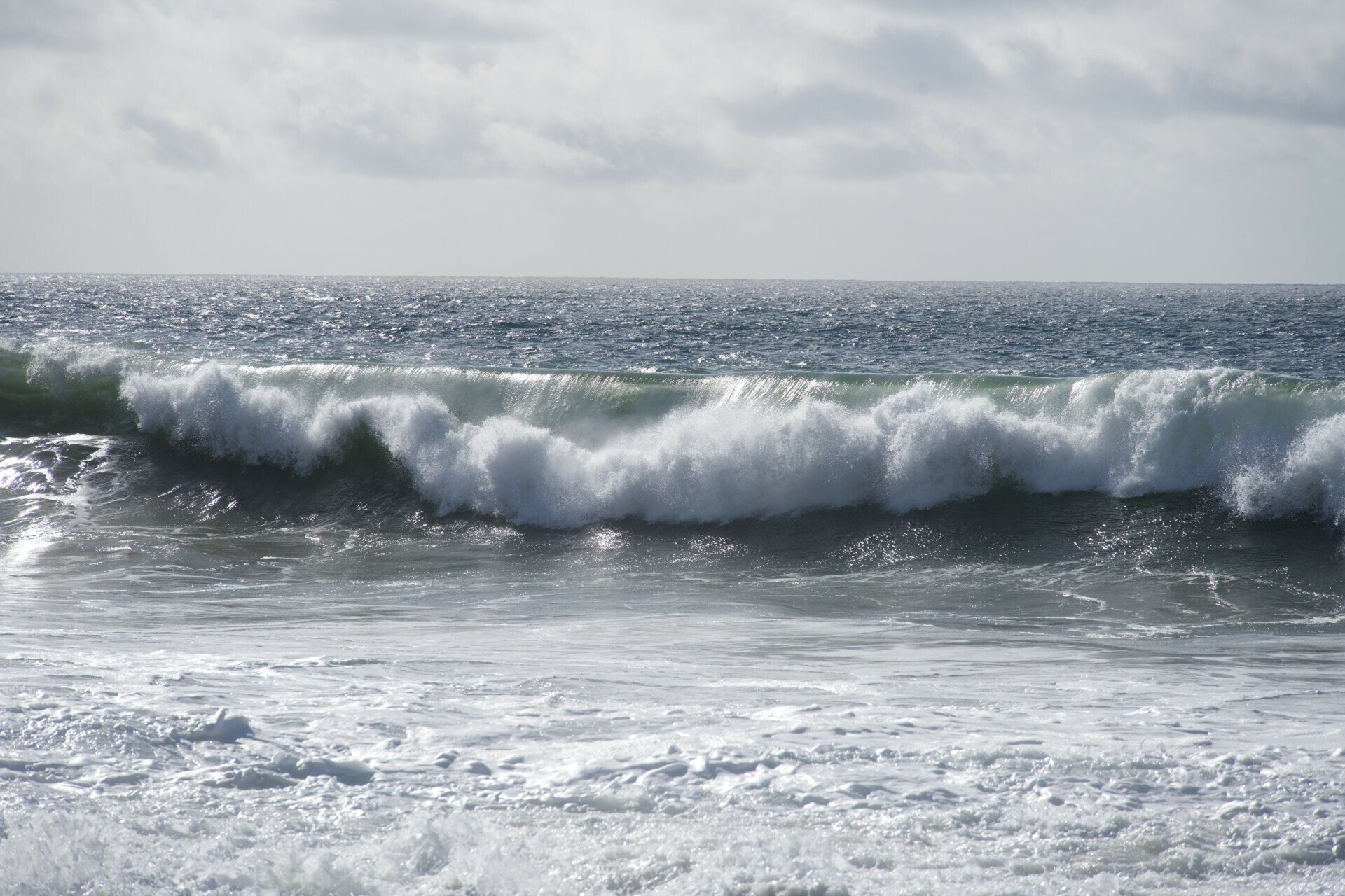A powerful wave cresting at Zuma Beach, Malibu, with the glistening Pacific Ocean in the backdrop.