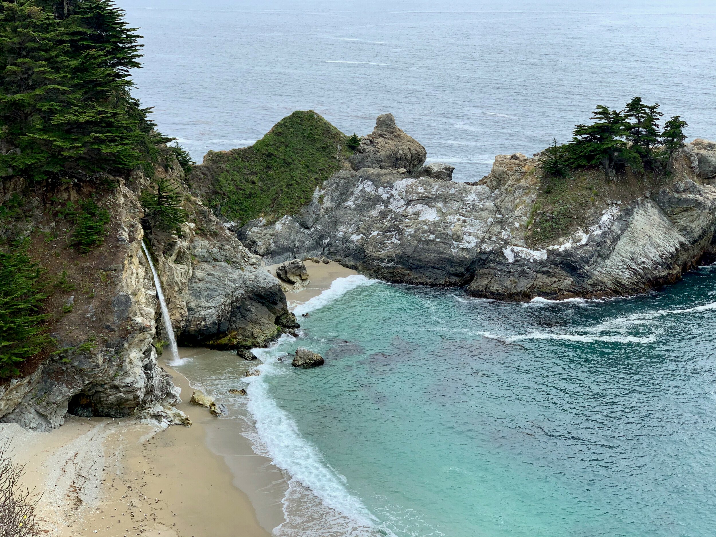 McWay Falls flowing into the turquoise sea surrounded by rugged cliffs and rich greenery, Big Sur, California