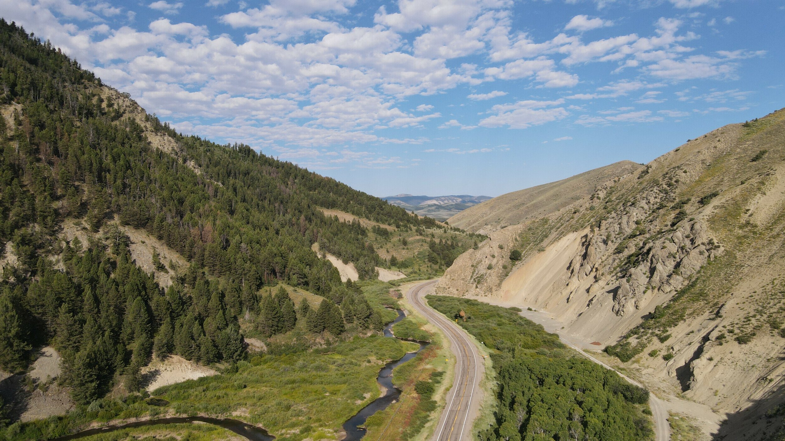 An aerial view of a road near a river at the Idaho-Wyoming border showcases the area's landscape of forests and open skies.