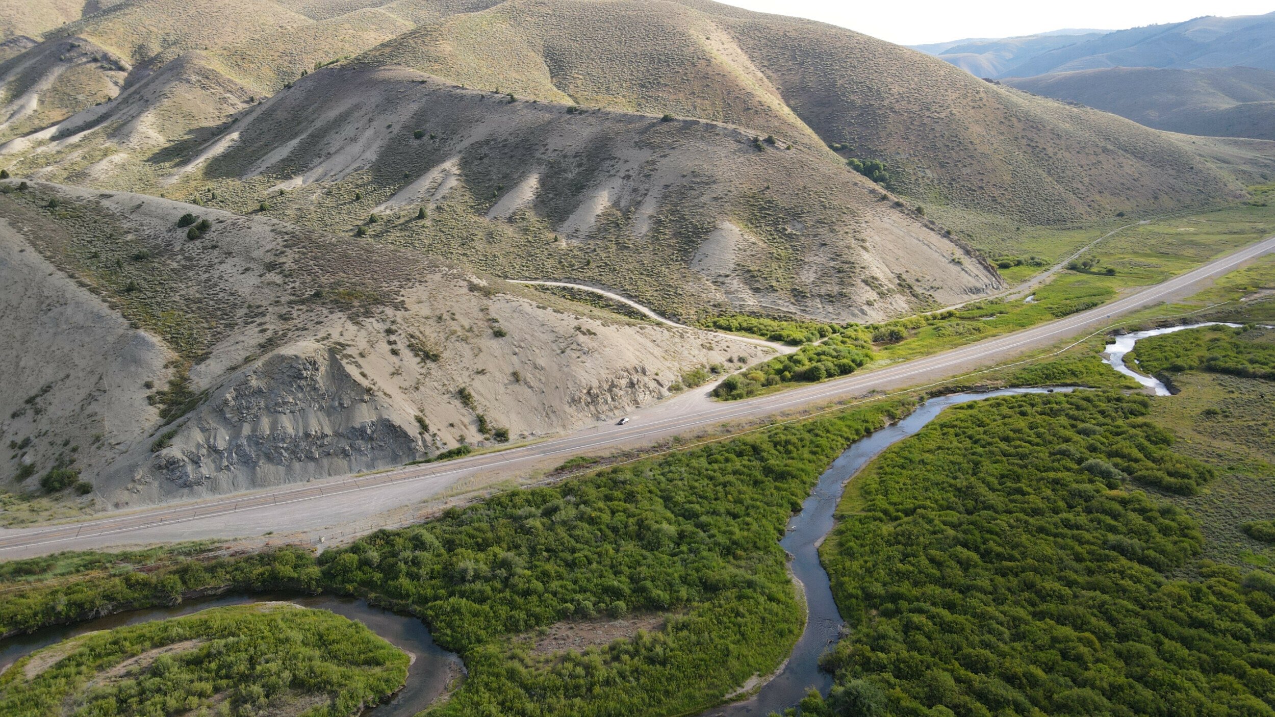 Aerial view of a winding road alongside a meandering creek at the border of Wyoming and Idaho.