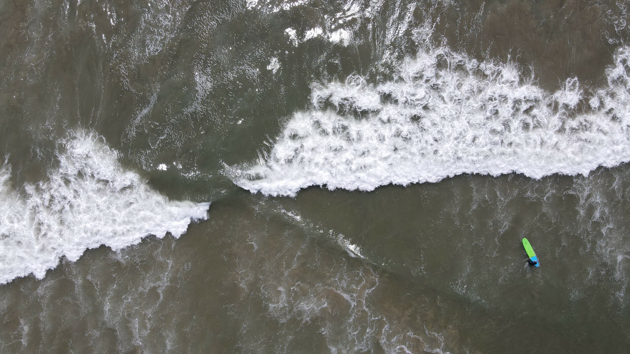 Aerial shot of a lone surfer amidst the foamy waves of Malibu Beach, captured by DJI Mavic Air 2.